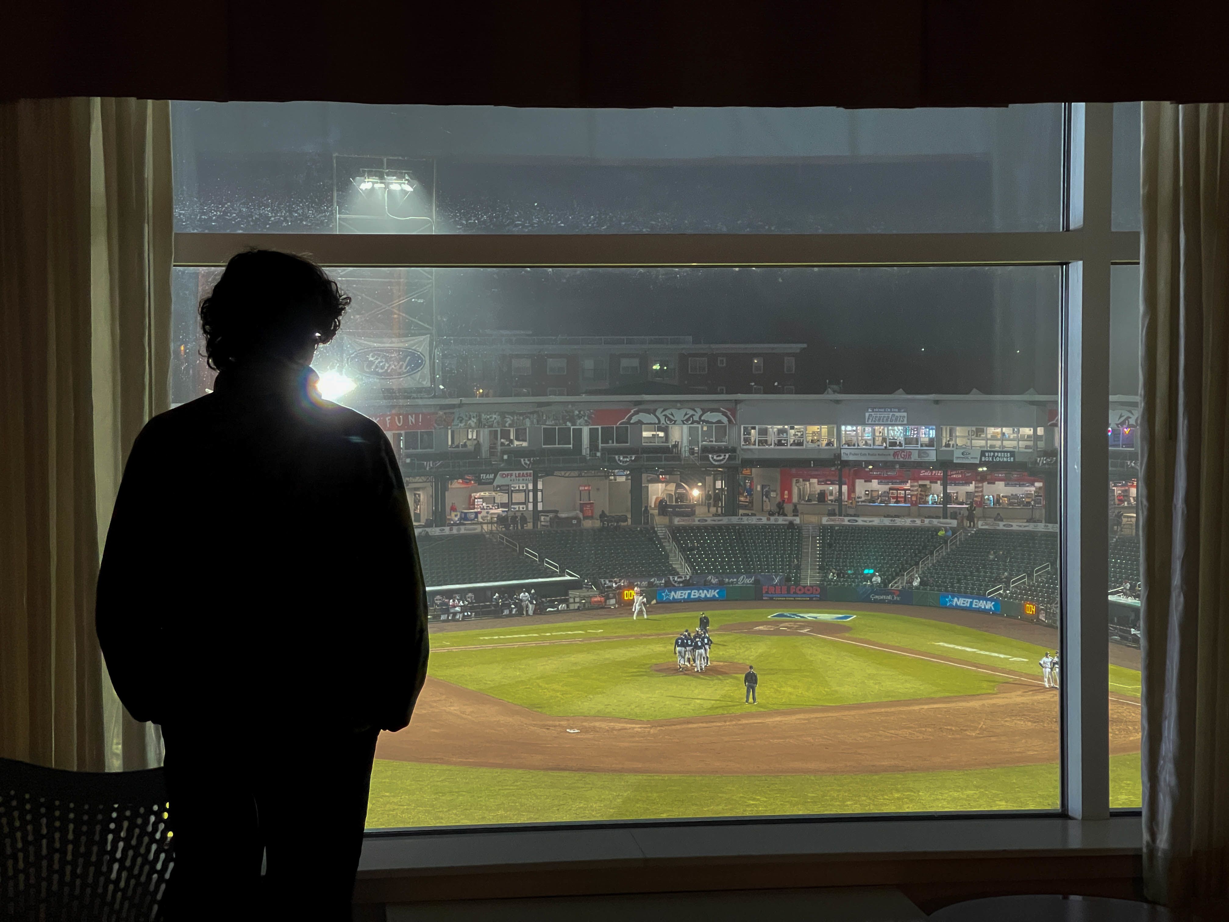 A person looks out a window at a baseball field.